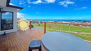 Una terraza de madera con una mesa y un adorno con forma de sol, con vistas a una zona costera y cielo despejado.
