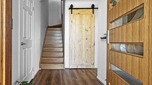 Un pasillo con una escalera de madera, una puerta corredera y una planta en maceta.