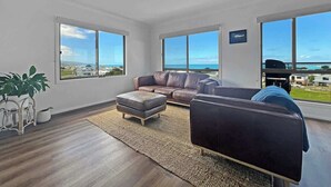 Una sala de estar moderna con un sofá de cuero, un reposapiés a juego y un amplio ventanal con vistas al océano.