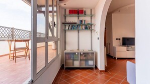 Una habitación con balcón, estantería, televisor y zona de comedor.