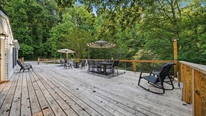 A wooden deck with outdoor furniture, including tables and chairs, surrounded by lush greenery. - Secluded 10-acre villa, sleeps 18, hot tub! (Trenton)