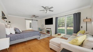 Ein Schlafzimmer mit Bett, Schreibtisch, Sessel, Sofa, Deckenventilator, Kamin und Fernseher.