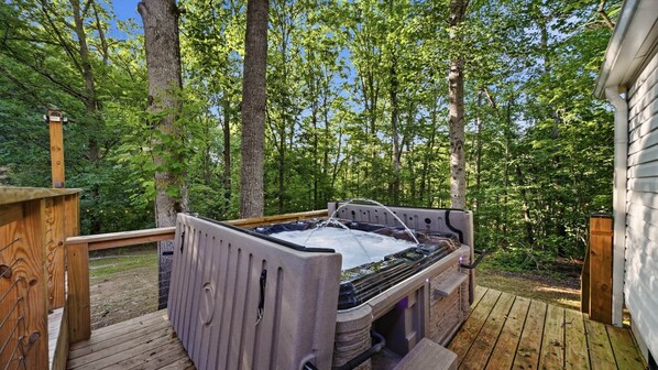 Ein Whirlpool auf einer Holzterrasse, umgeben von Bäumen.
