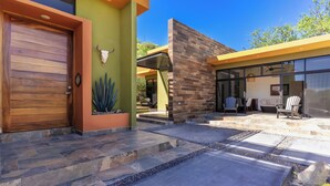 A modern house with a wooden garage door, a stone pathway, and a patio area with chairs and a table. - 5BR/5B bath Los Barriles Retreat w/ Pool, Hot Tub & Sea of Cortez Views (Buenos Aires)