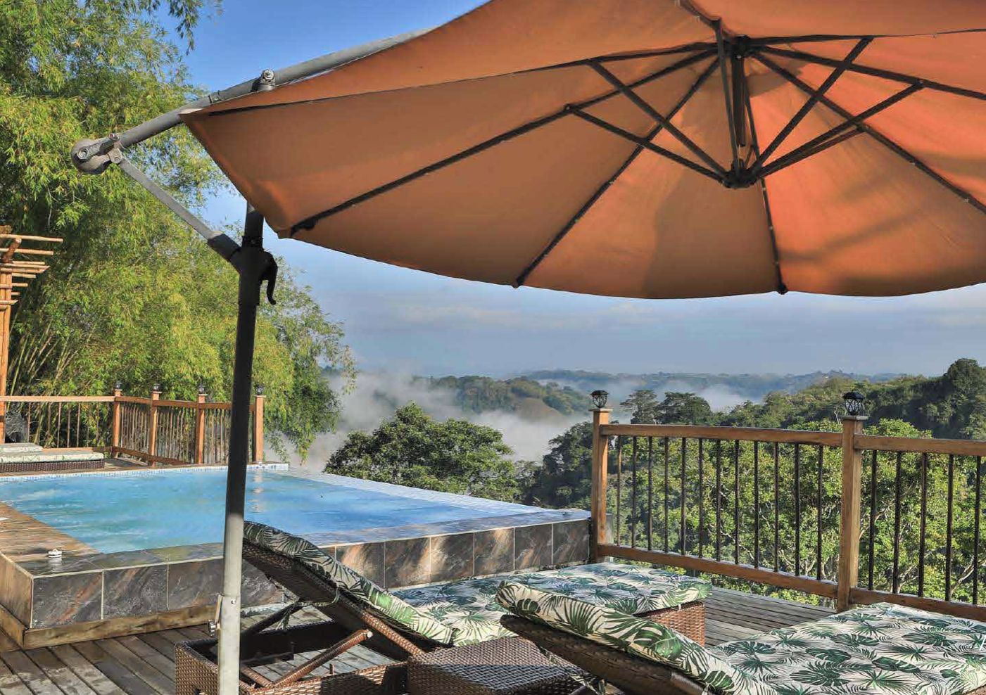 Uma área de piscina com um deck de madeira, cadeiras de descanso e um grande guarda-sol.