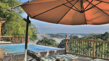 Uma área de piscina com um deck de madeira, cadeiras de descanso e um grande guarda-sol.