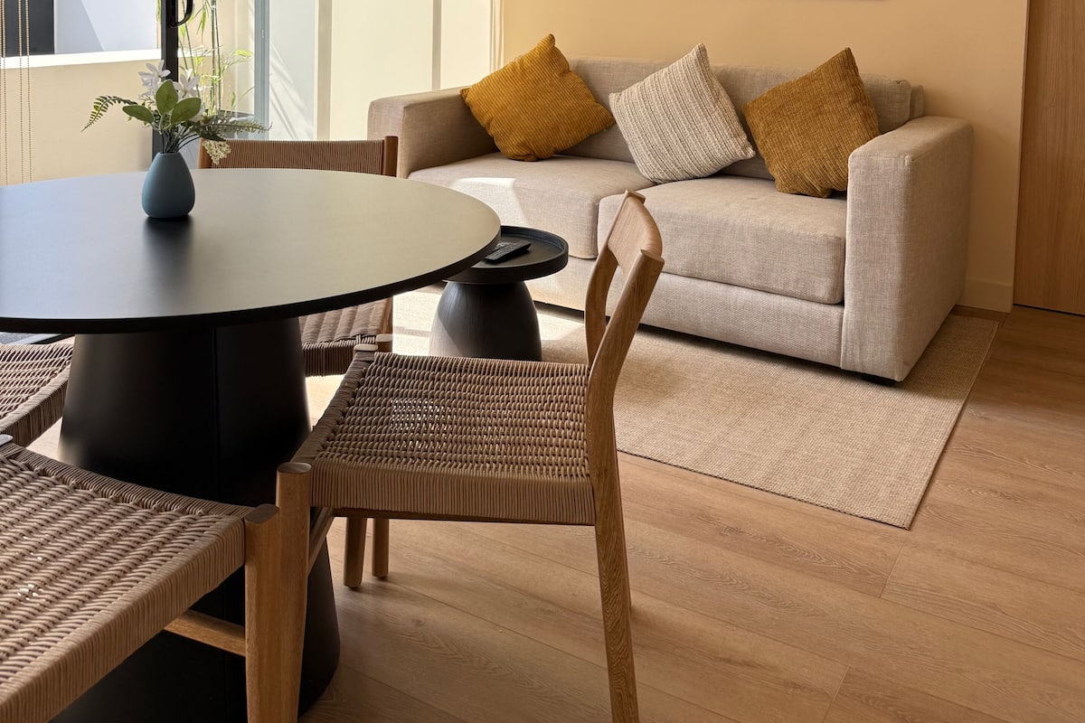Una sala de estar moderna con una mesa redonda, un sofá y un amplio ventanal.