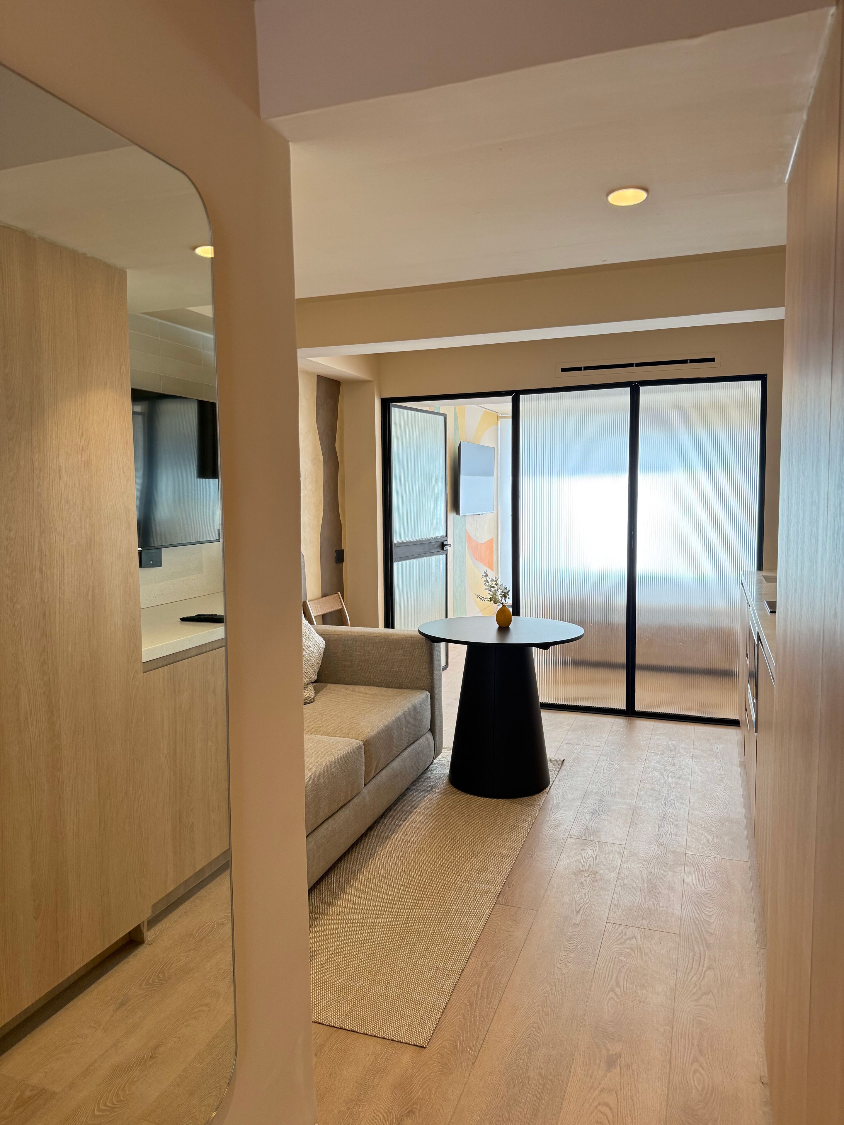 A modern hotel room with a sofa, a round table, and a large window with blinds.