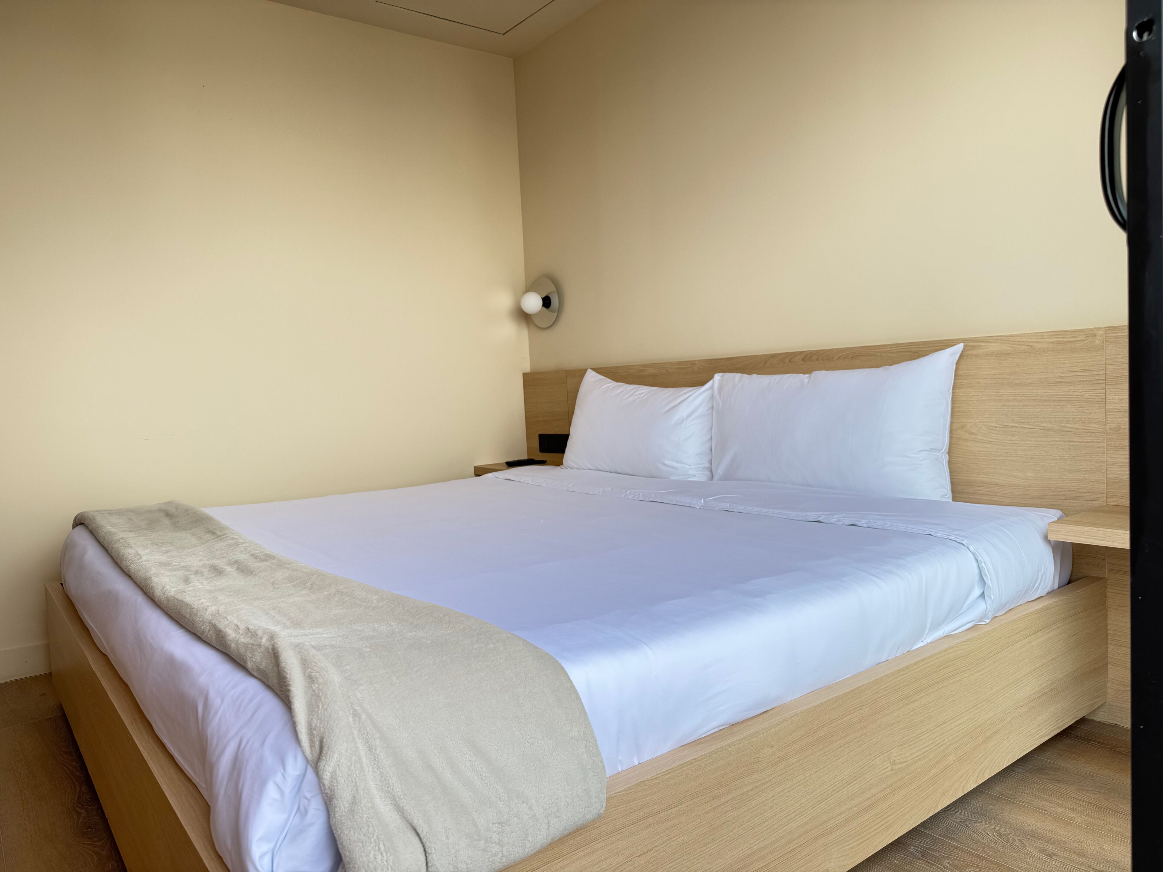 Ein Einzelbett mit Holzbettrahmen, weißer Bettwäsche und einer beige farbenen Tagesdecke.