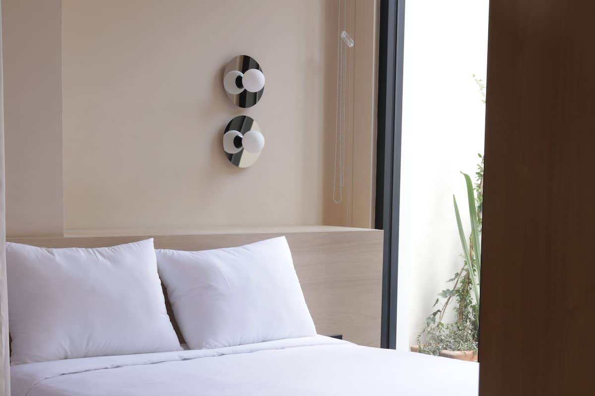 Un dormitorio moderno con cabecera de cama de madera, ropa de cama blanca y un adorno colgante en la pared.