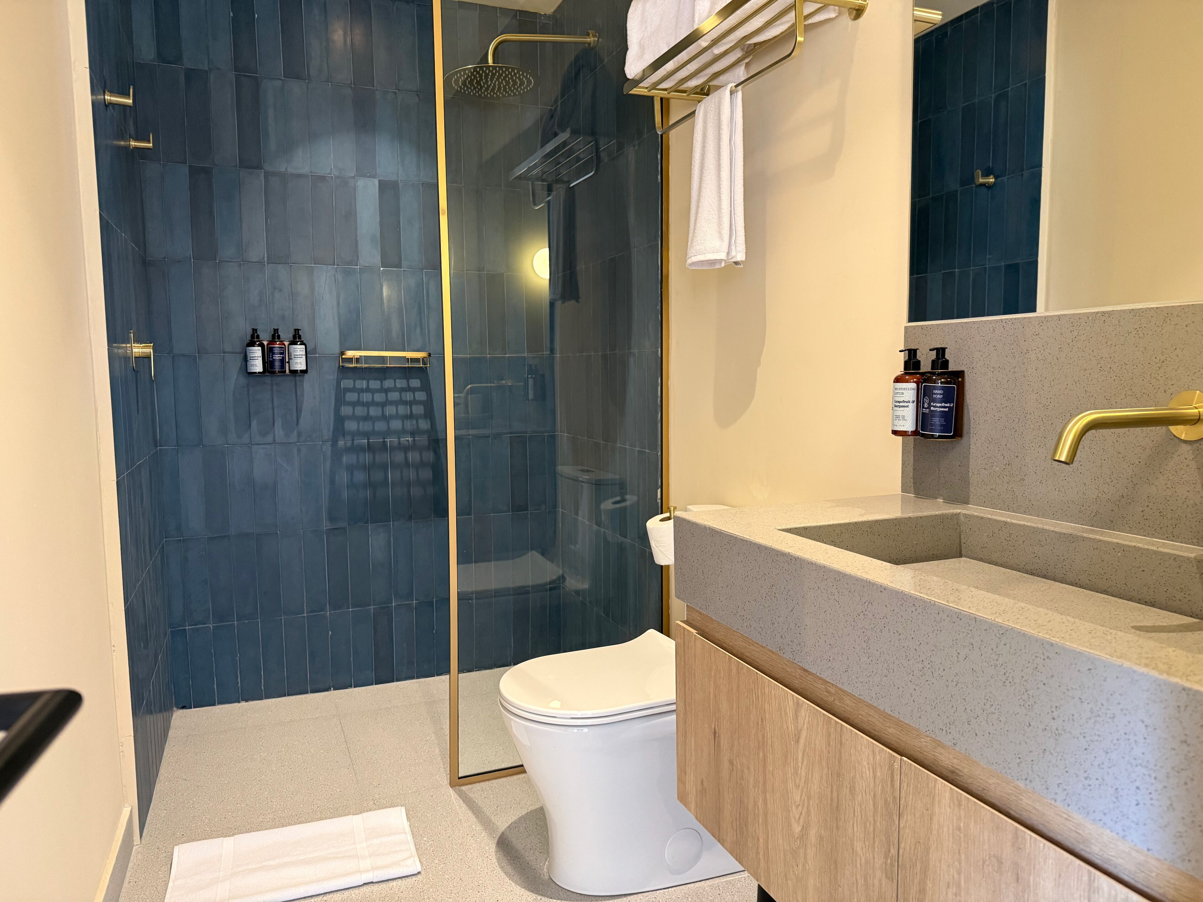 Een moderne badkamer met een glazen douchecabine, een wit toilet, een granieten aanrechtblad en een gouden kraan.