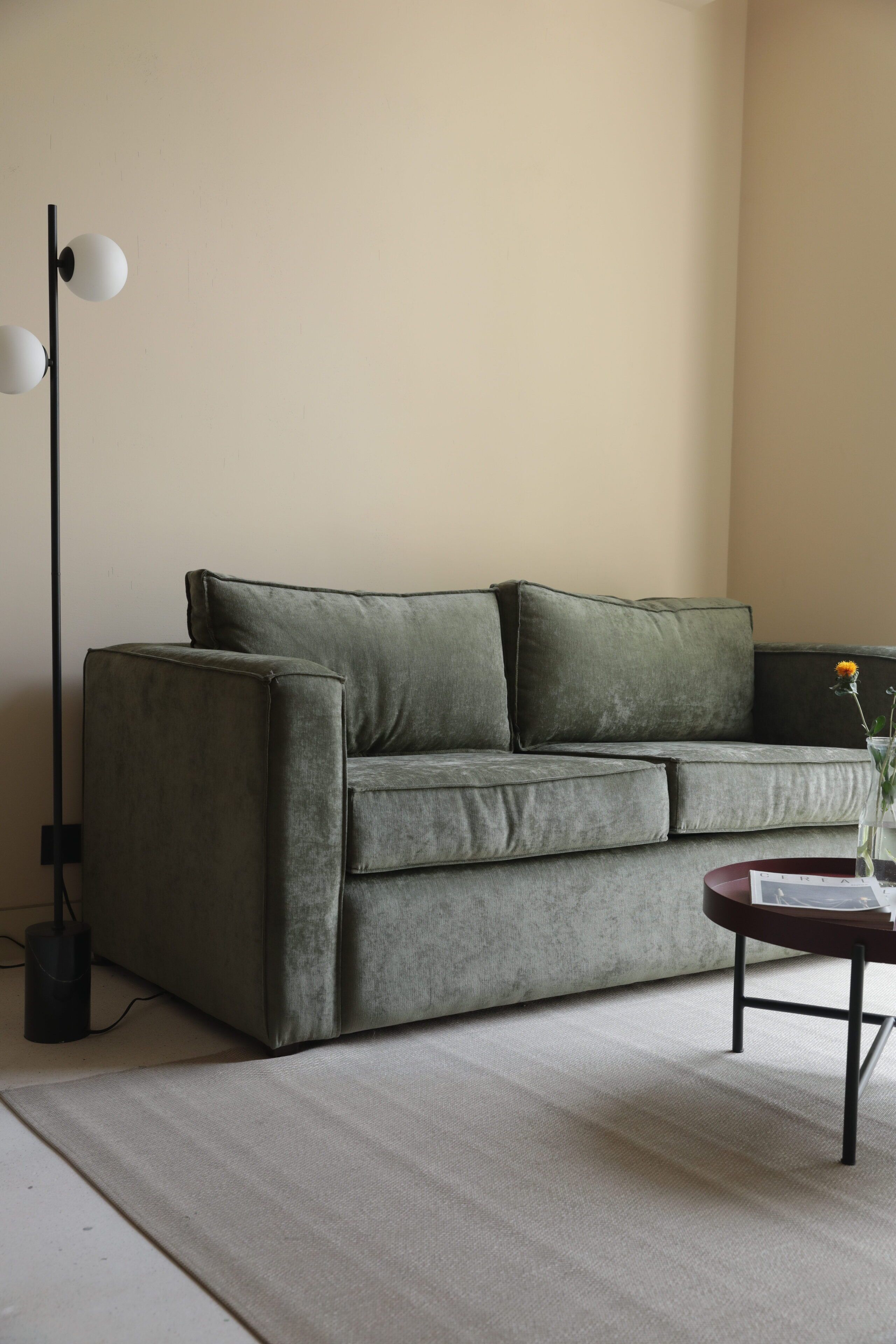 A modern living room with a grey sofa, a floor lamp, and a small table with a vase.