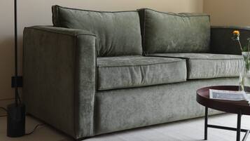 A modern living room with a grey sofa, a floor lamp, and a small table with a vase.