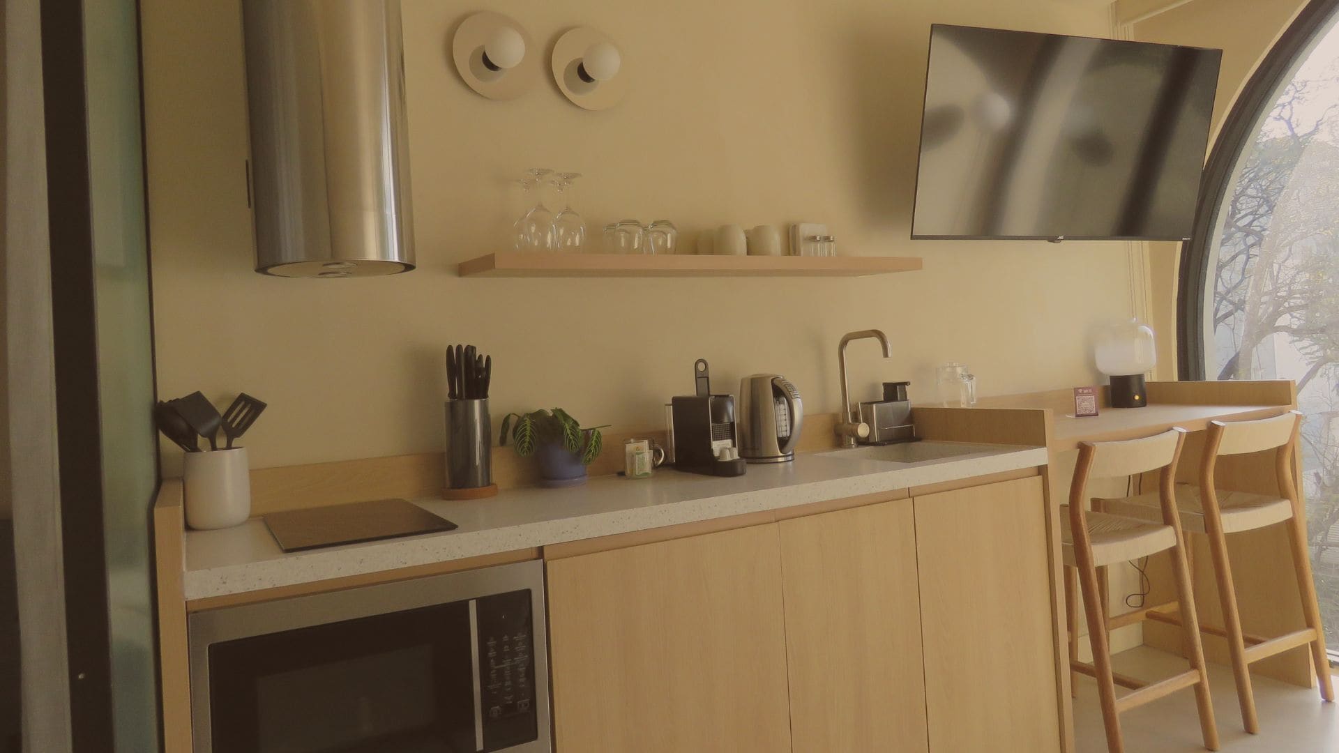 Une cuisine moderne dotée d’une hotte en acier inoxydable, d’un téléviseur à écran plat fixé au-dessus du plan de travail et d’un îlot central en bois avec des tabourets de bar.