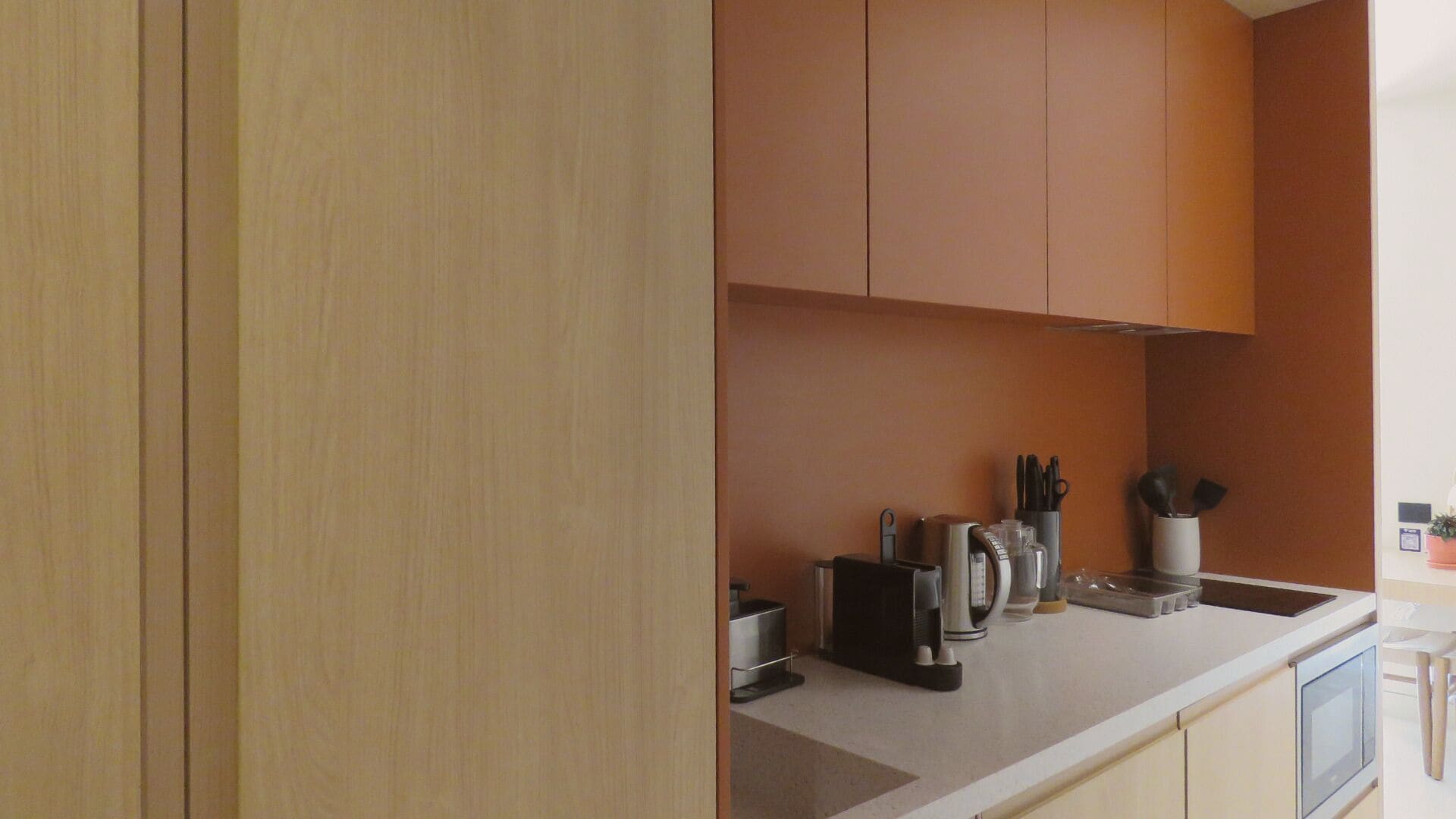 Una cocina moderna con armarios de madera clara, encimera blanca y diversos electrodomésticos.