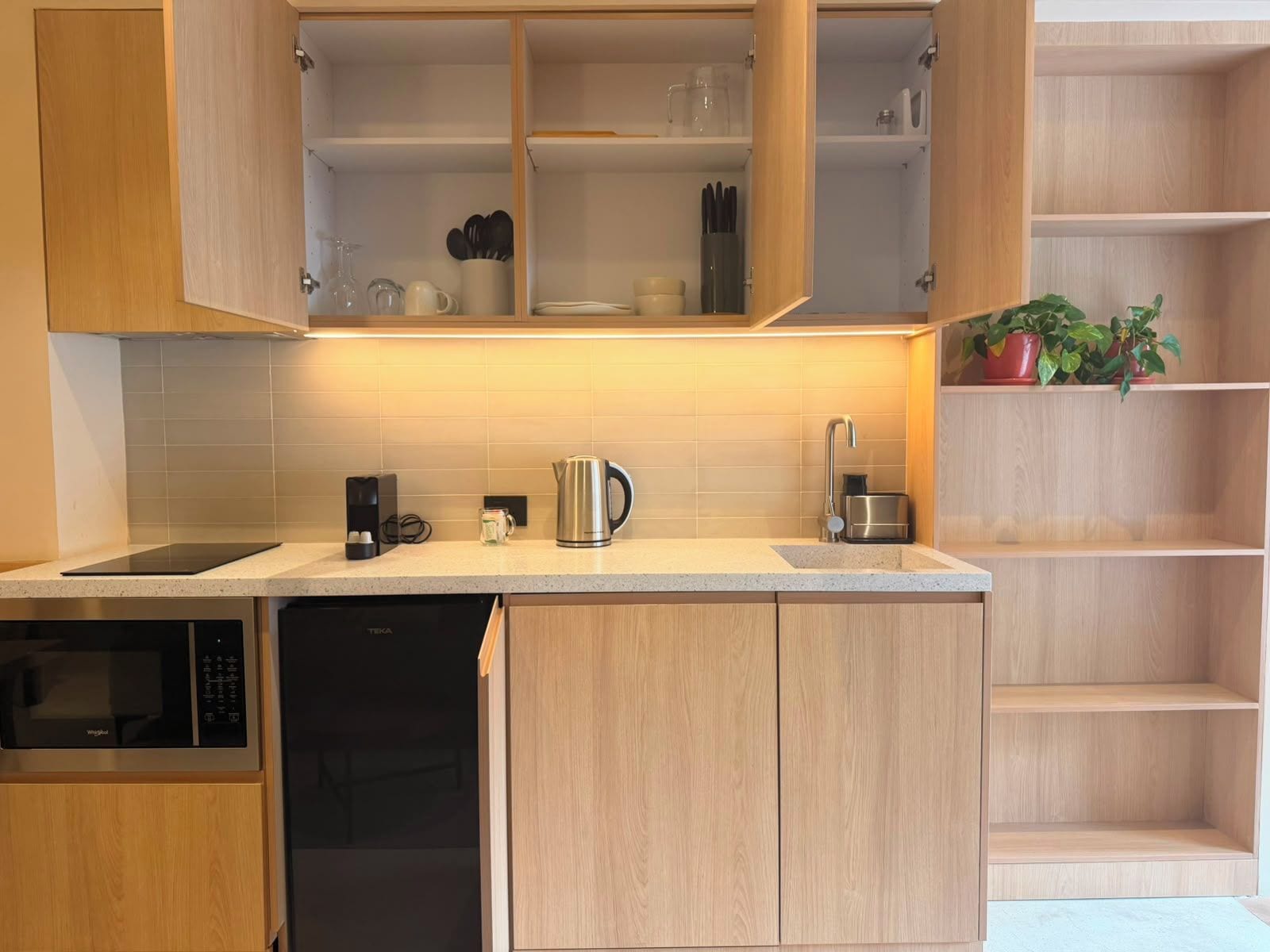 A modern kitchen with wooden cabinets, a dishwasher, a coffee maker, and a kettle.