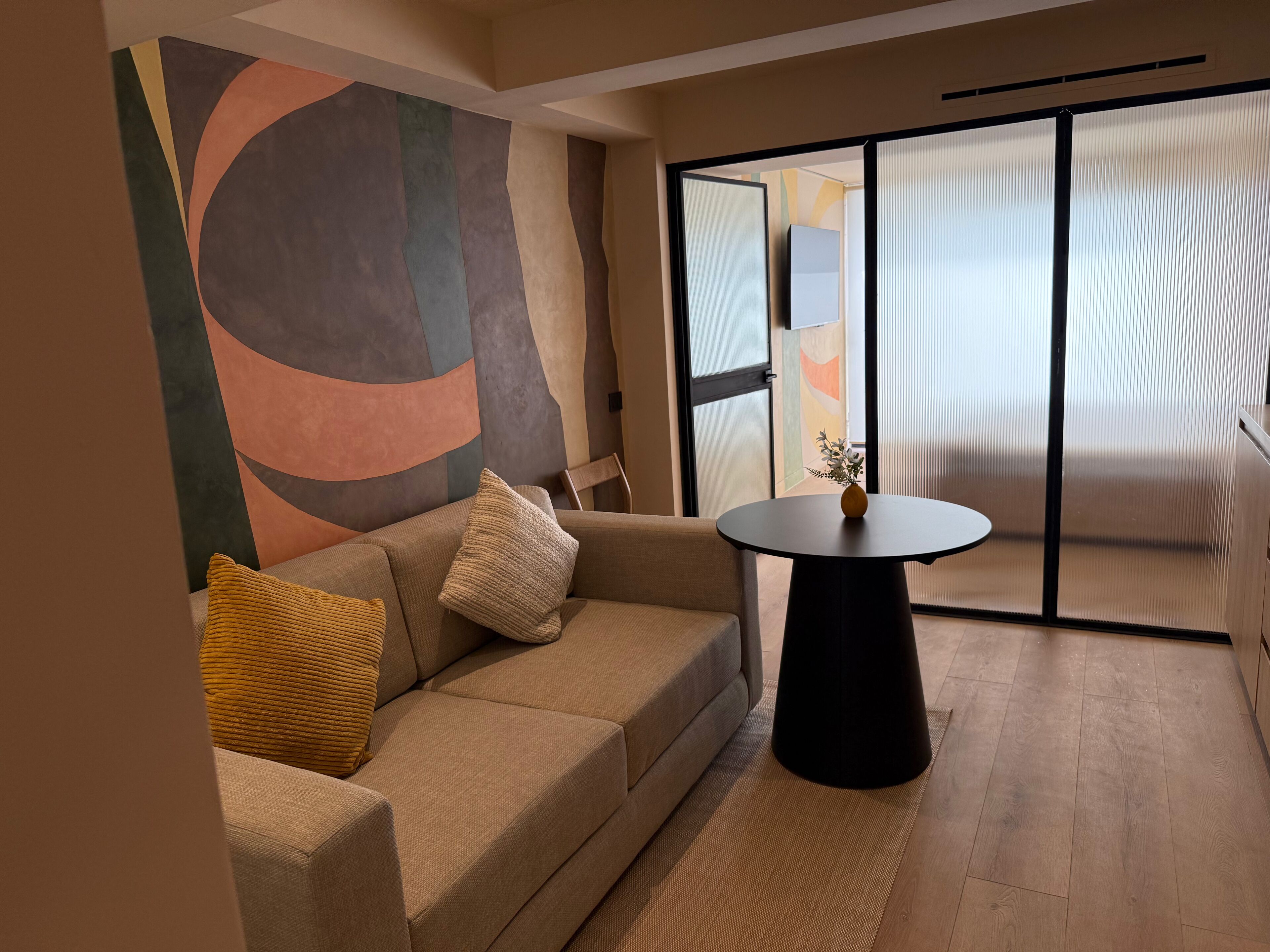 A modern living room with a sofa, a round table, and a view through a glass door.