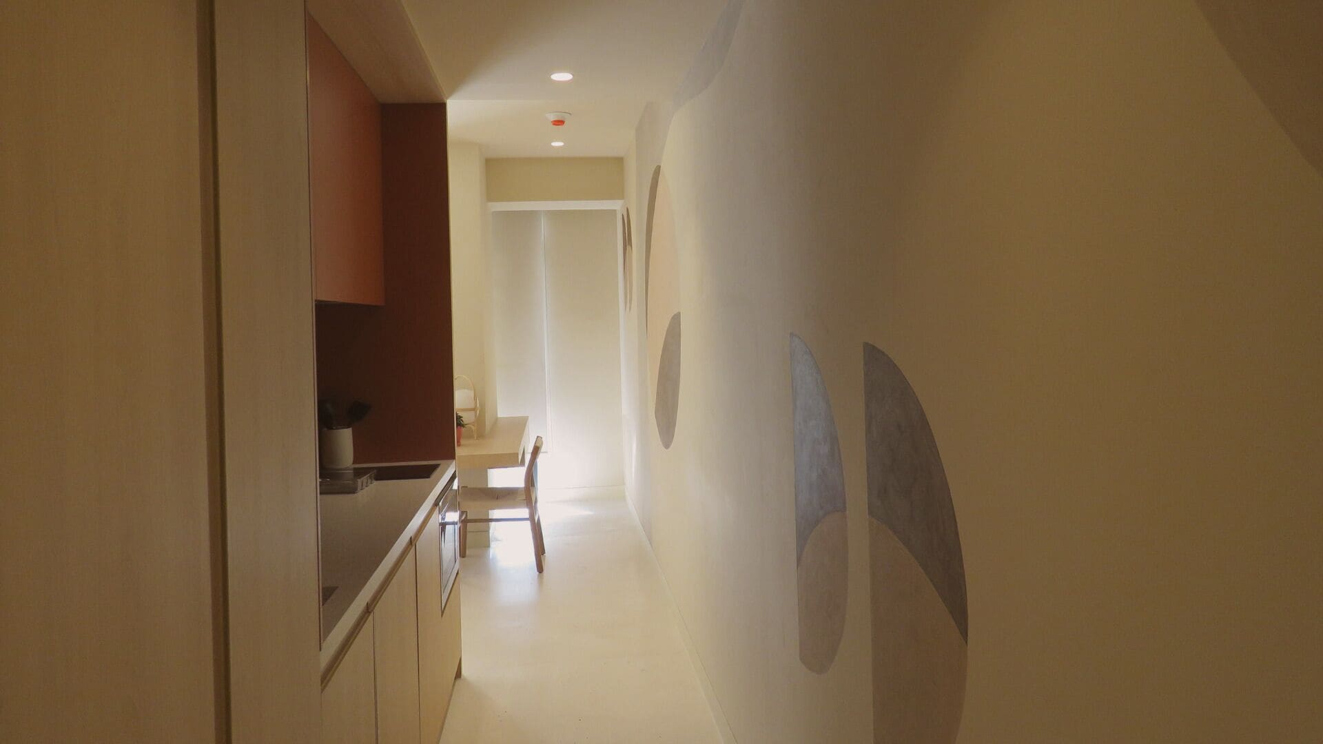 Un couloir étroit, avec un coin cuisine sur la gauche, une table à manger au centre et un mur orné d’ouvertures circulaires sur la droite.