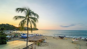A beach with a palm tree, beach umbrellas, and a small building. - Maramara Playa Beach Hotel (Sayulita)