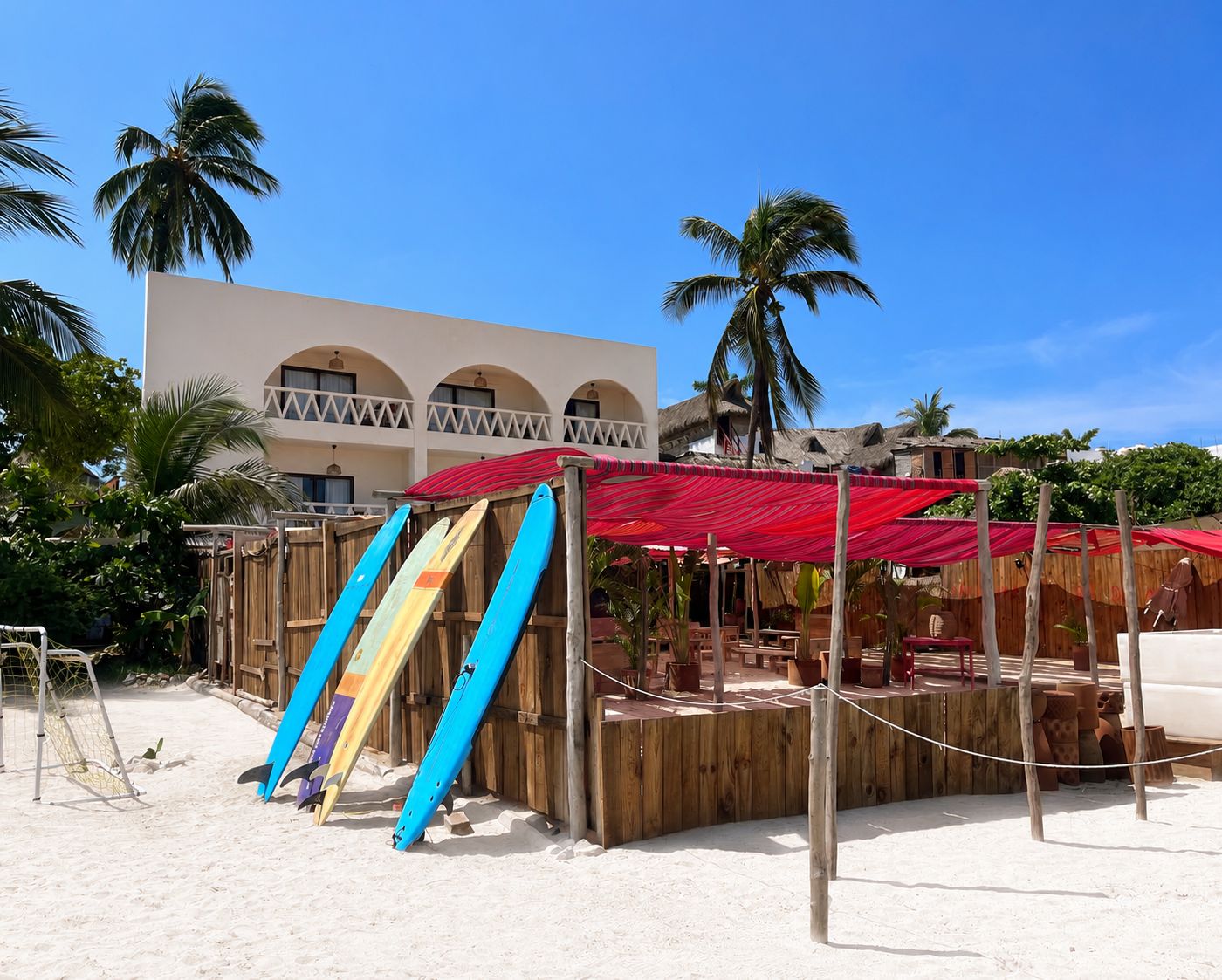 A beachside area with a wooden structure, a red canopy, and several surfboards leaning against it.