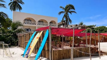 A beachside area with a wooden structure, a red canopy, and several surfboards leaning against it.