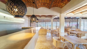 A restaurant with a long counter, wooden tables, wicker chairs, and patterned ceiling lights. - Maramara Playa Beach Hotel (Sayulita)