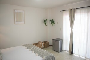 Quarto com cama, um frigorífico pequeno e janela com cortinas.