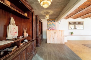Un mostrador de recepción de madera con un colorido mural en zigzag, una lámpara colgante y una planta en maceta.