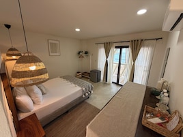 Un dormitorio con cama, lámparas de noche, mesitas de noche, cómoda, escritorio pequeño, silla, ventana con cortinas y vistas al exterior.