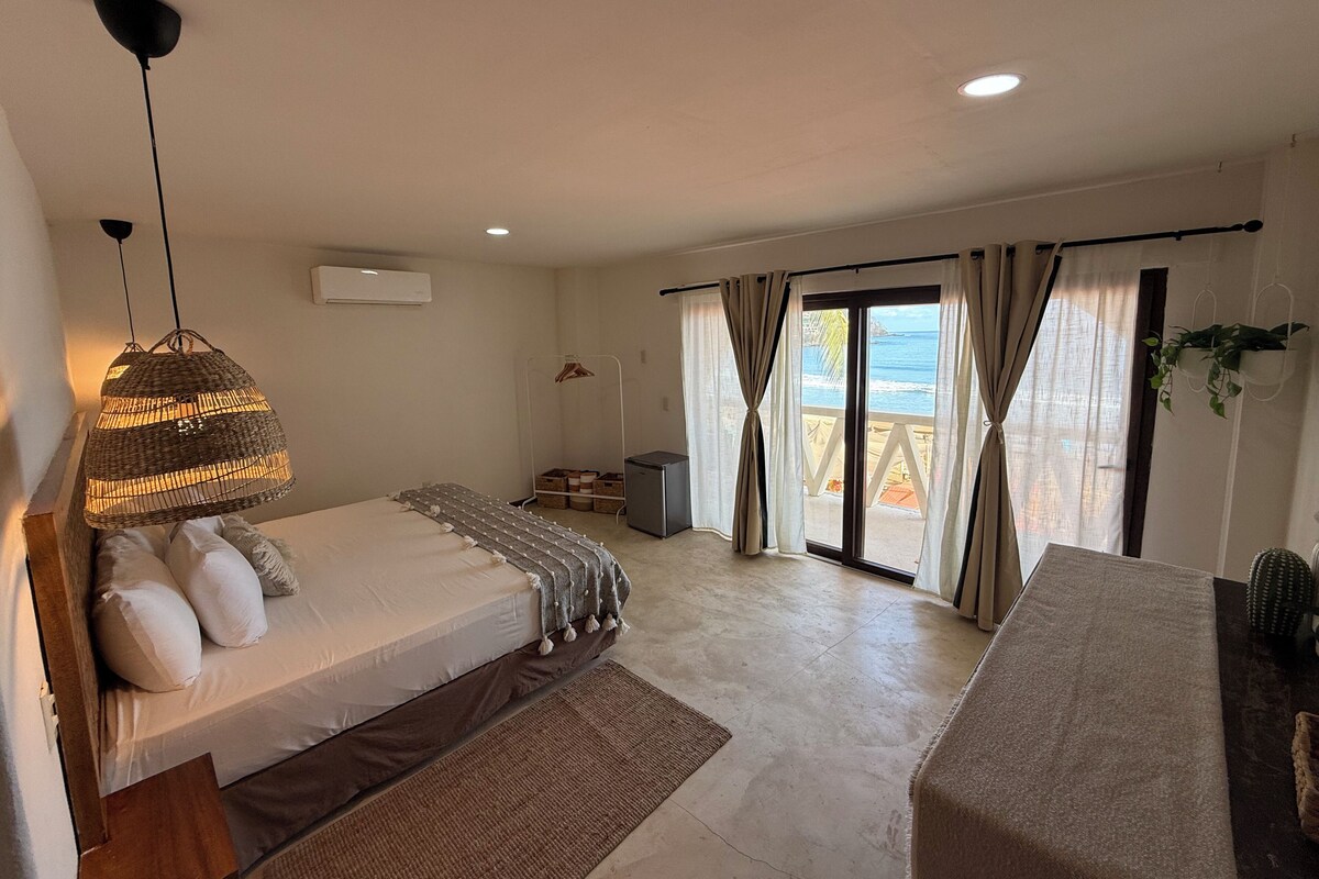 Een slaapkamer met een bed, een hangende lamp, een bureau en uitzicht op de oceaan door het raam.