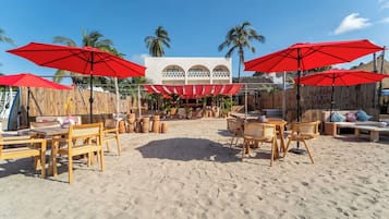 A beachside outdoor seating area with wooden furniture and red umbrellas.