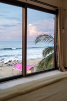 Vista desde una ventana sobre una playa con sombrillas y palmeras.