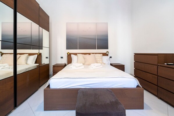 A modern bedroom with a large bed, wooden wardrobe, and a large mirror.