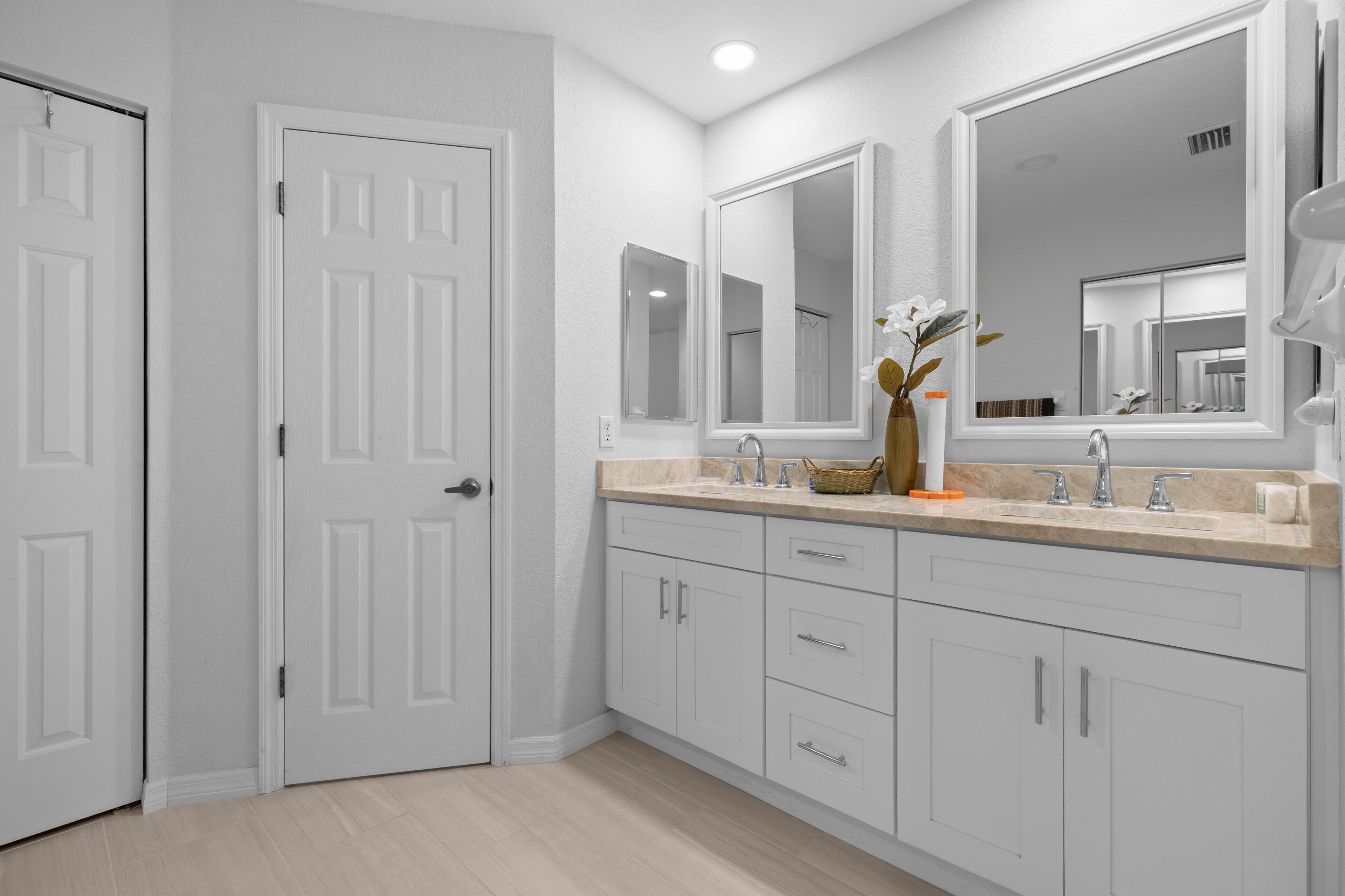 A modern bathroom with white cabinetry, a large mirror, and a vase with flowers.