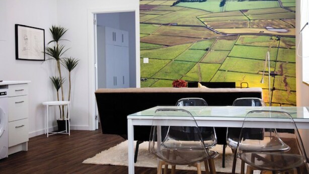 Eine moderne Küche mit einem großen Fenster, einem Essbereich mit Glastisch und Blick auf eine grüne Landschaft.