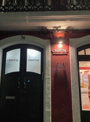 A building entrance with two doors labeled "CRISTAL APARTAMENTOS" and the number "56" above them.