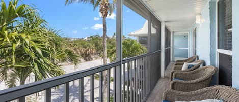 A balcony with wicker furniture and a view of the beach and palm trees.