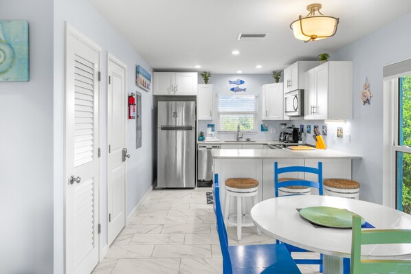 A modern kitchen with white cabinets, a stainless steel refrigerator, and a dining area with blue chairs and a white table.