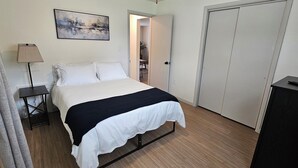 Une chambre à coucher avec un lit, une lampe de chevet, un tableau au mur et une porte donnant sur une autre pièce.