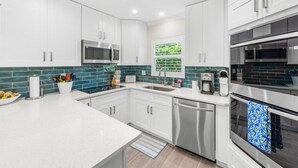 A modern kitchen with white cabinets, stainless steel appliances, and a teal backsplash.