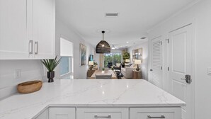 A modern kitchen with white cabinetry, a marble countertop, and a pendant light.