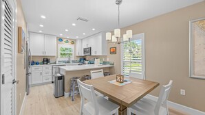 A modern kitchen with white cabinetry, a wooden dining table, and a chandelier. - SeaShells Unit 40 – Island Getaway with Pool, Pickleball & Beach Access (Sanibel)