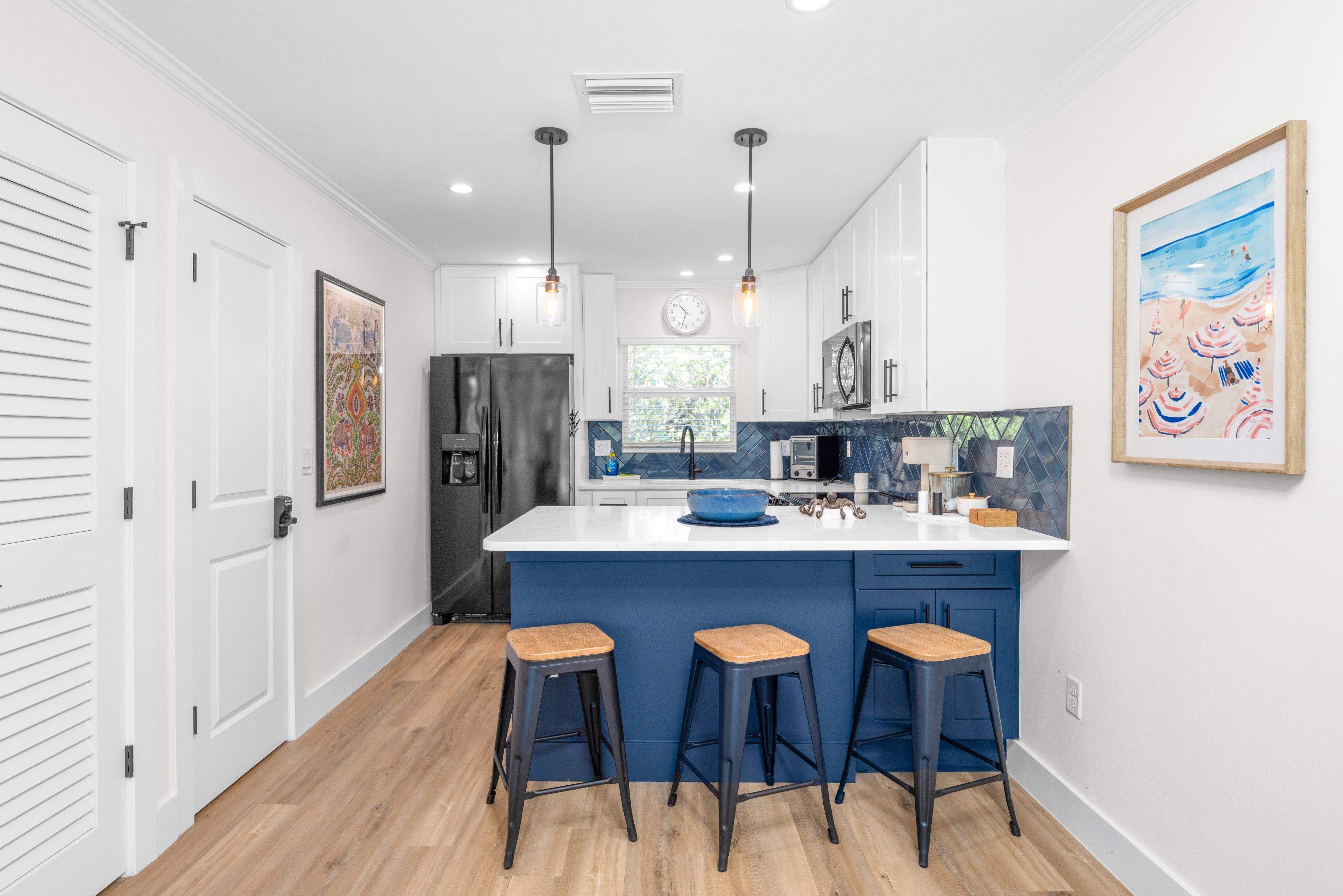 A modern kitchen with a central island, bar stools, and pendant lighting.