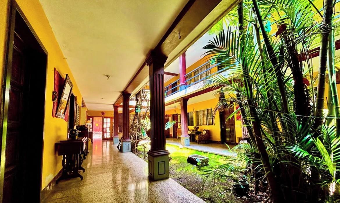 A corridor with a covered walkway, potted plants, and a view of a building with balconies.