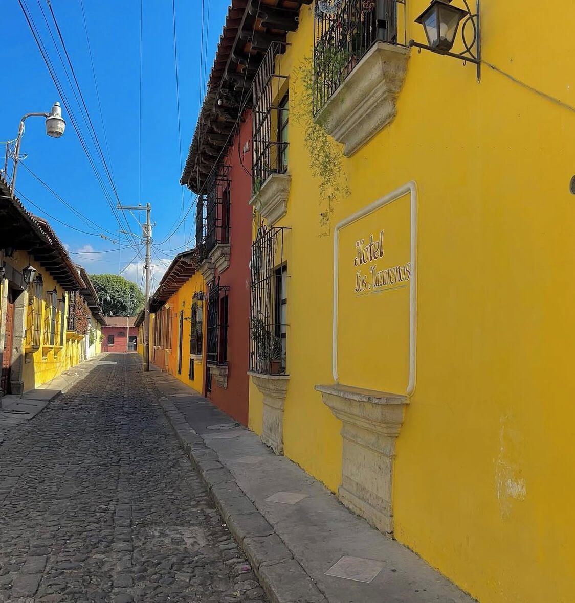 A cobblestone street lined with colorful buildings, including a yellow building with a sign for 'Hotel Los Zarcillos.'