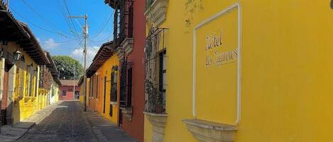 A cobblestone street lined with colorful buildings, including a yellow building with a sign for 'Hotel Los Zarcillos.'