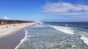 A beach with waves, a sandy shore, and buildings in the background. - Shell Yeah! Oceanfront, Indoor Pool (Myrtle Beach)