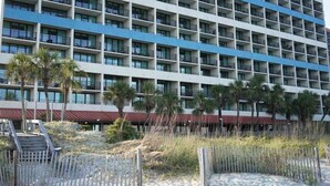 A multi-story hotel with balconies, a beach in the foreground, and palm trees. - Shell Yeah! Oceanfront, Indoor Pool (Myrtle Beach)