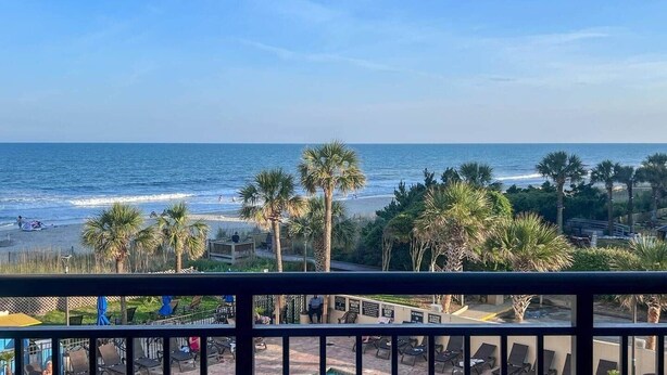 A beach view with palm trees, a sandy shore, and a clear sky. - Shell Yeah! Oceanfront, Indoor Pool (Myrtle Beach)