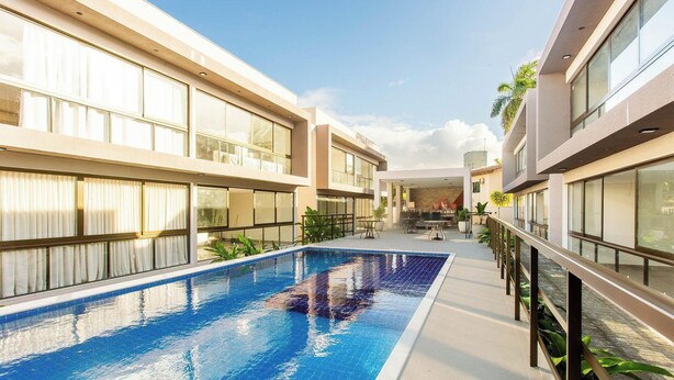 Un hotel moderno con piscina central, ventanas amplias y una zona de estar cubierta al aire libre.